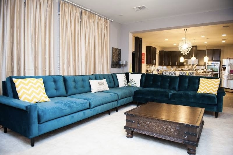 Open living space with a teal velvet sectional, an eat-in kitchen and a kitchen beyond