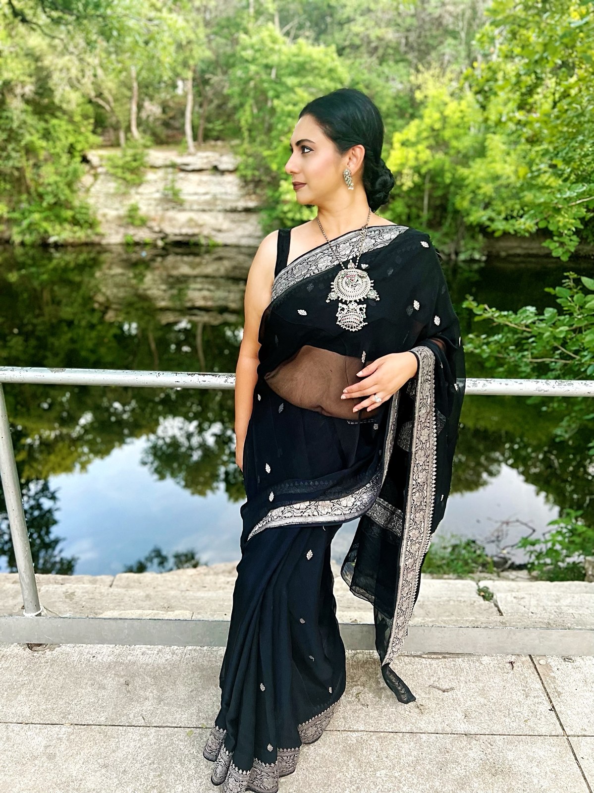 Founder in a black saree with a silver border beside a pond